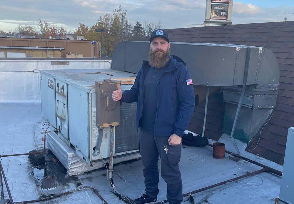 Mr. Fridge technician facing the camera beside rooftop HVAC equipment