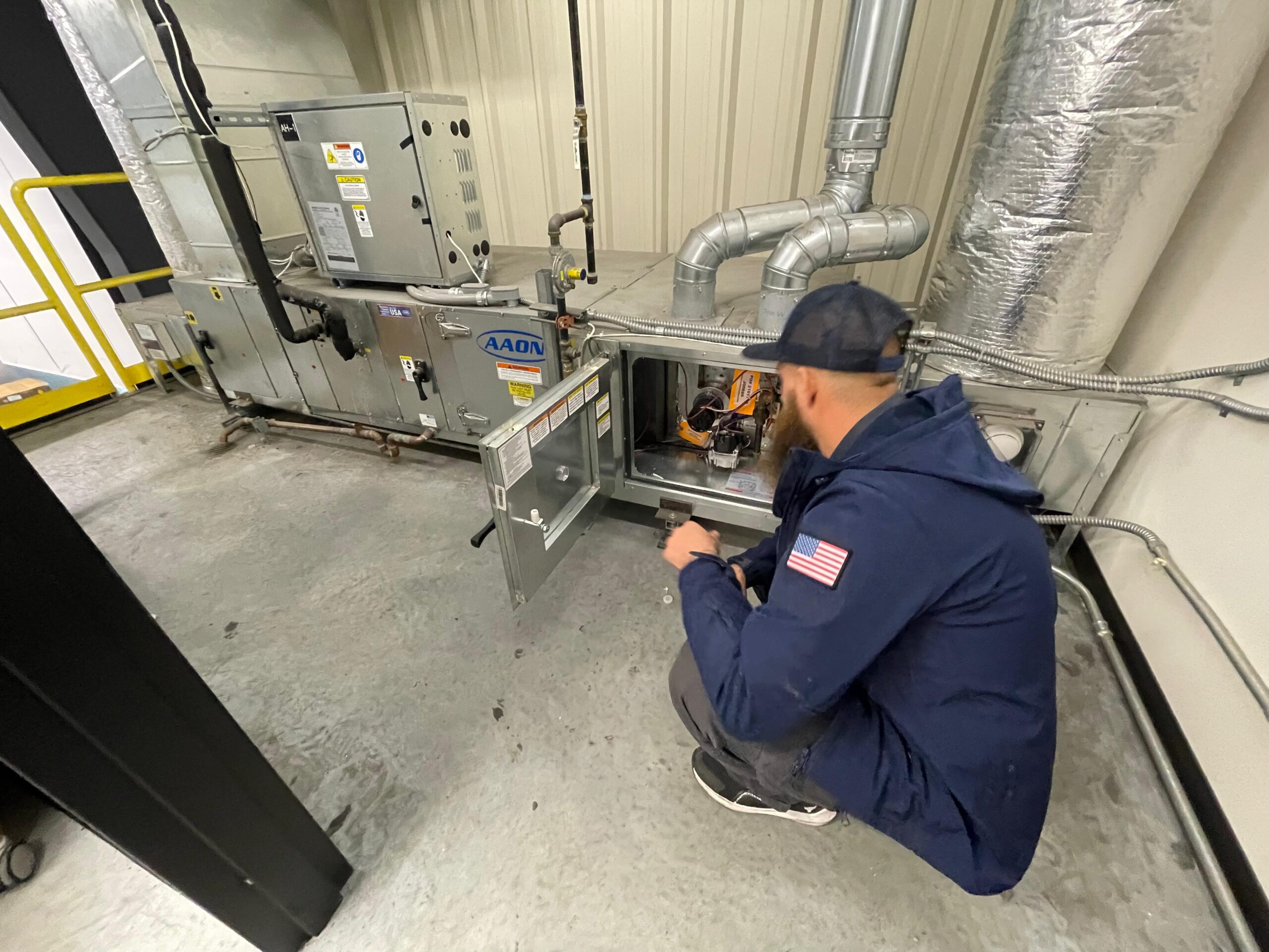 Technician inspecting indoor HVAC equipment and duct connections