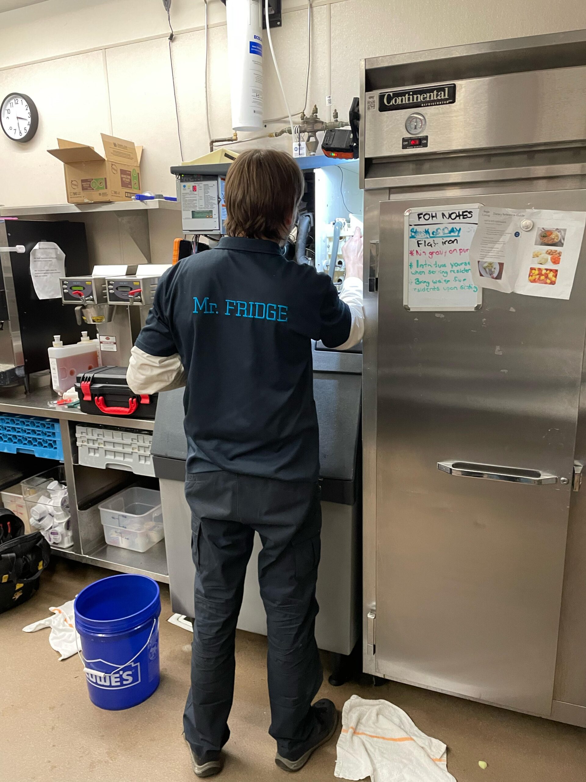 Mr. Fridge technician servicing an ice machine beside a stainless steel refrigerator