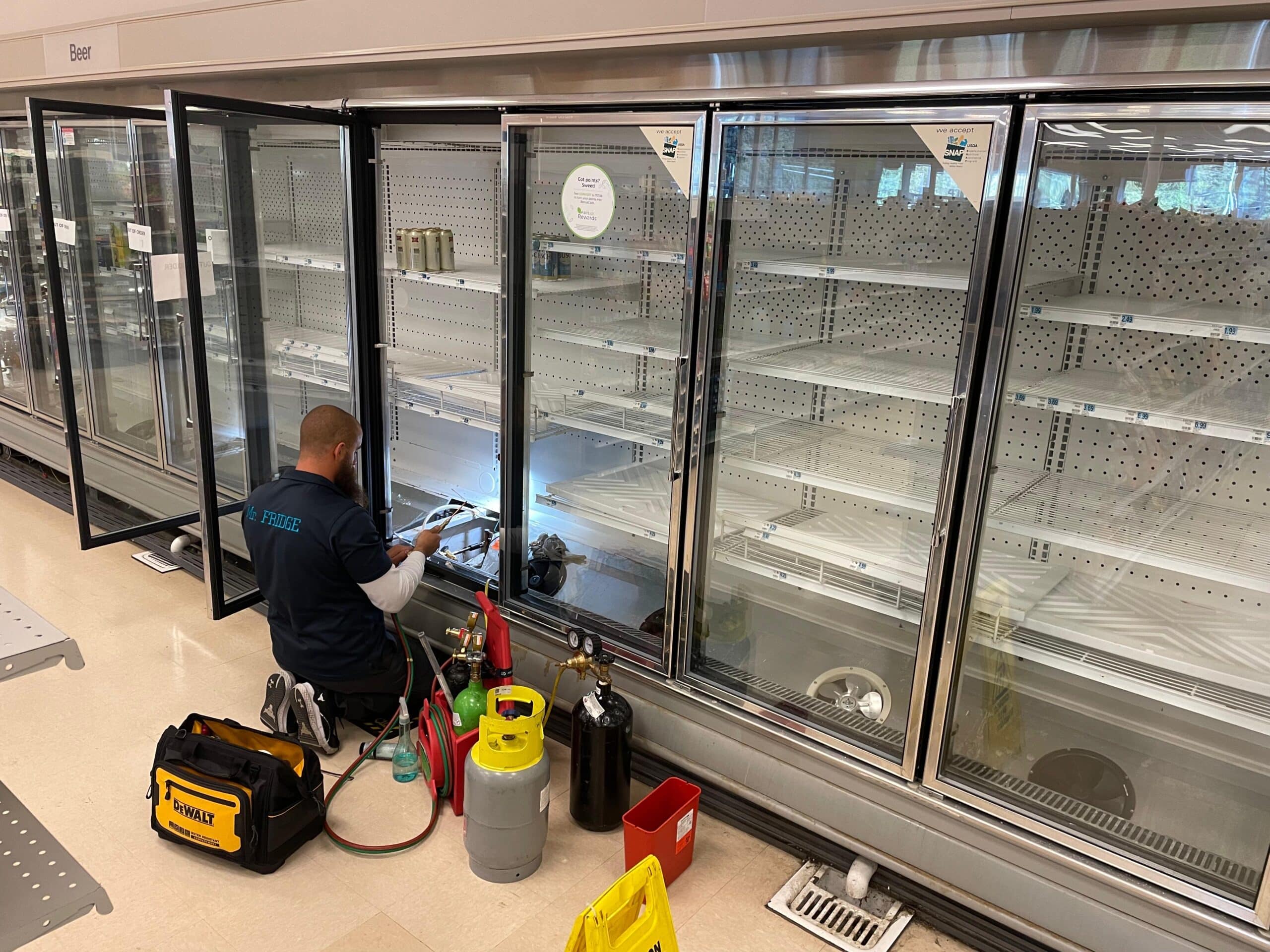 Technician working beside an open glass-door refrigerated display case