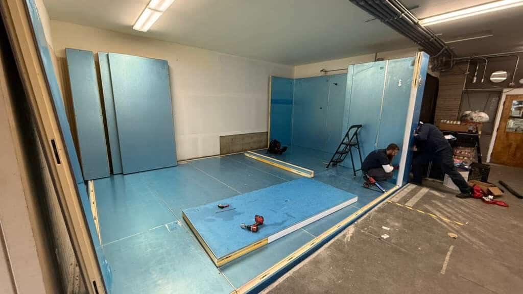 Technicians fitting insulated wall and floor panels during walk-in cooler construction