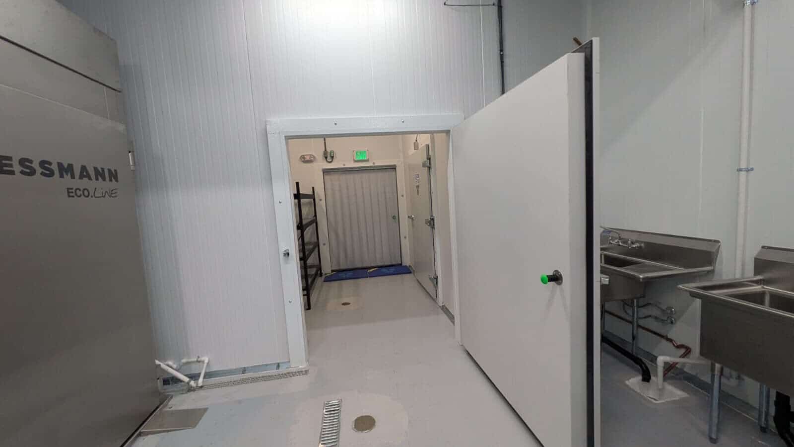 Open insulated walk-in cooler door beside stainless steel food-preparation equipment