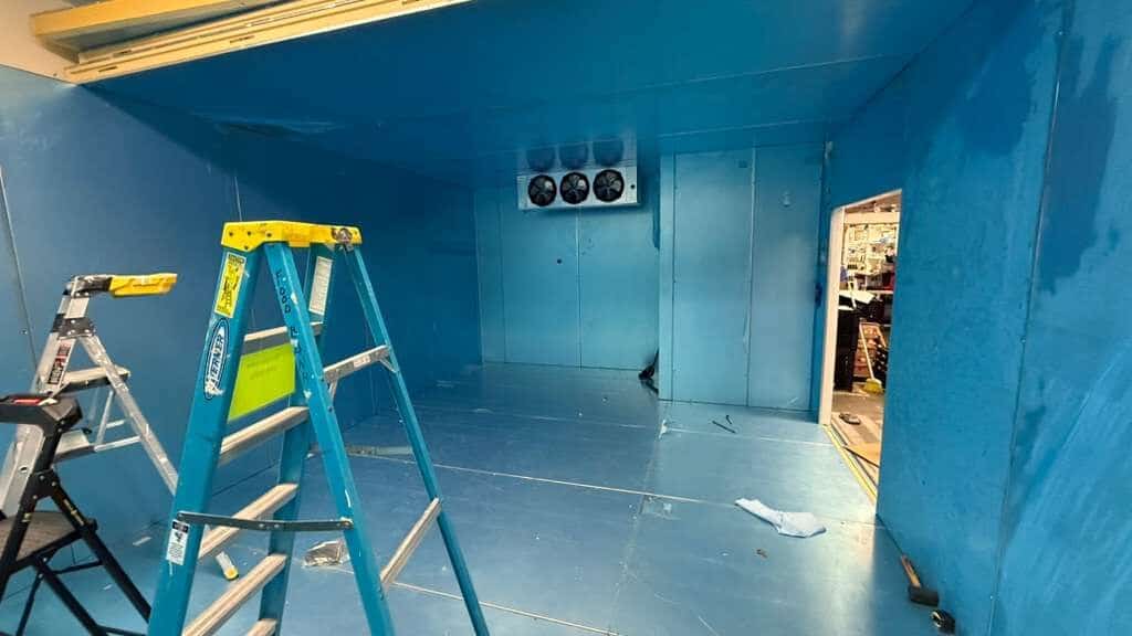 Walk-in cooler interior with ceiling-mounted evaporator fans and a ladder