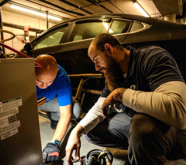 Two technicians inspecting a refrigeration compressor assembly